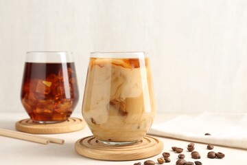 Tasty iced coffee with milk and beans on white table