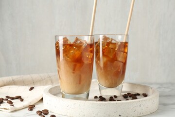 Tasty iced coffee with milk and beans on white marble table