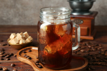 Tasty iced coffee, sugar, grinder and beans on wooden table, closeup