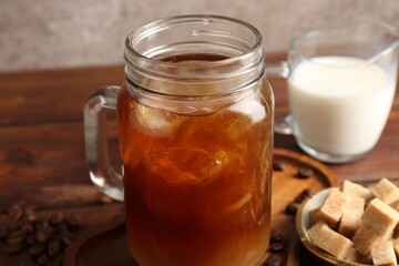 Tasty iced coffee, milk, sugar and beans on wooden table, closeup