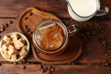 Tasty iced coffee, milk, sugar and beans on wooden table, flat lay