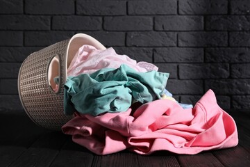 Overturned laundry basket with clothes on black wooden surface