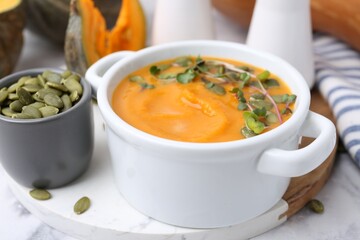 Delicious pumpkin soup with seeds and microgreens in bowl on table, closeup