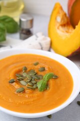 Delicious pumpkin soup with seeds and basil in bowl on table, closeup