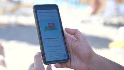 The video demonstrates essential travel planning as hands download local maps for offline access while at the beach, ensuring navigation capability without internet connection. 