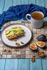 slices of toasted whole-wheat bread topped with sliced avocado , served with figs, walnuts and tea, on a colorful mosaic background