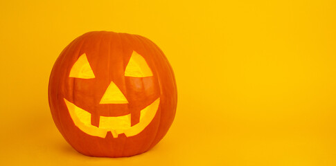 Carved pumpkin with a smiling face illuminating a vibrant orange backdrop