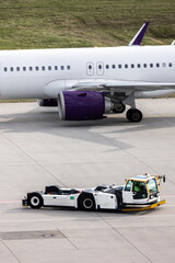 Modern regional jet aircraft towed by ground vehicle on airport taxiway tarmac under sunlight. Engine cockpit clearly visible crew performs technical operations before next scheduled flight airport