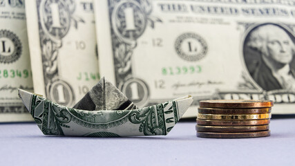 Creative use of one dollar bill folded into a boat beside stacked coins