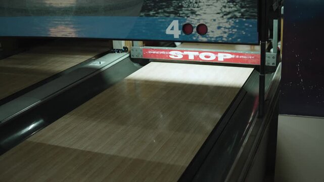 Bowling ball hits pins and ball gate with stop sign closes. Real automated safety system in old bowling alley with shabby, worn stop sign on gate.