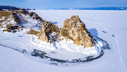 Aerial view of snowy rocky island, ice fragments and blue sky over frozen lake