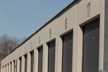 Fototapeta premium row beige storage doors under blue sky, quiet minimalist facade with repetitive garage bays, long shadows, clean concrete pavement, ideal for lastmile logistics and delivery staging