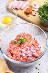 Raw minced meat with onion, parsley, spices and egg on grey table, closeup