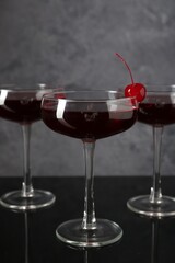 Glasses of tasty cocktails with garnish on mirror surface, closeup