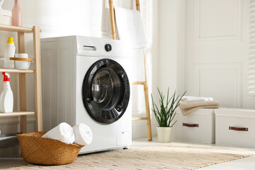 Washing machine, detergents, towels and houseplant in laundry room. Interior design
