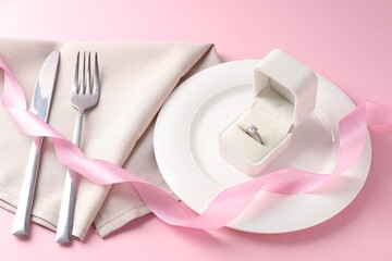 Beautiful table setting for romantic dinner and box with engagement ring on pink background