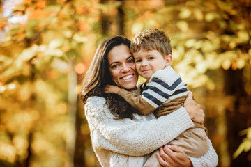 young mother with son in her arms in autumn in beautiful forest