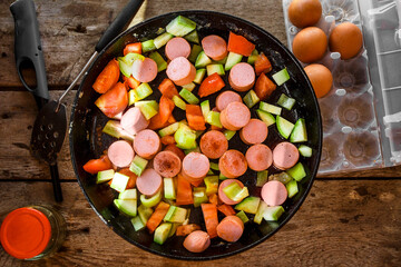 Homemade breakfast with sausages, tomatoes, eggs and zucchini in a frying pan
