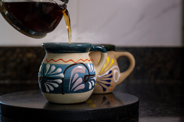 Hot coffee pouring into a steaming traditional mexican jarrito, with another jarrito in background