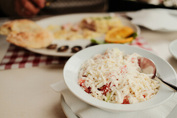 Traditional Balkan shopska salad made of tomato, cucumber, and grated cheese served in a white bowl on restaurant table