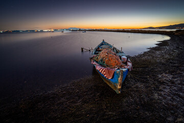 Blue fishing boat with nets on shore at sunset