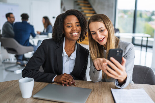Businesswomen colleagues sharing content on smart phone in office