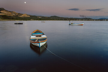 Small fishing boats floating on calm water under full moon