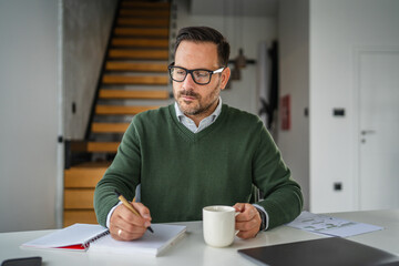 Focused man in glasses writing notes at home office