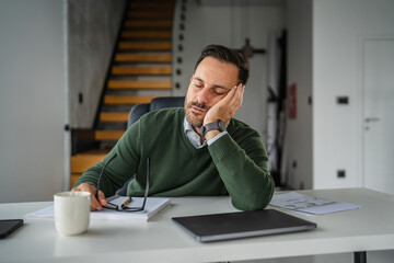 Tired businessman sleeping at office desk feeling burnt out