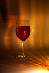 Elegant wine glass filled with red liquid on a warm golden-yellow background. Abstract lighting creates a luxurious and artistic mood, perfect for concepts of celebration, elegance, and nightlife.