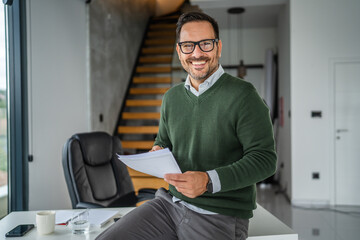 Mature man thinking while holding documents in modern office