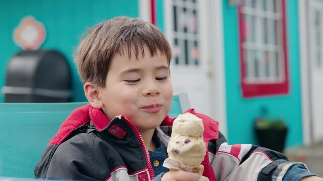 Smiling boy in a red jacket enjoying an ice cream cone outdoors on a cool day