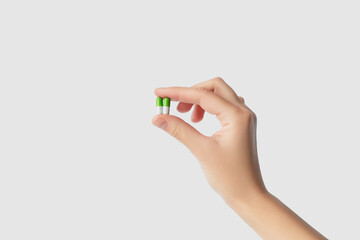 Hand holding two small green and white medicine capsules isolated on light gray background