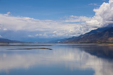 Tranquil view of Yarlung Tsangpo River near Tsetang in Lhoka (Shannan), Tibet, reflecting distant Himalayan mountains and clouds in calm, pristine waters.