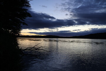 A panoramic view of a sunset over a wilderness lake in the Adirondacks with red and gold colors.