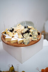 Assortment of cheeses on a wooden plate with olives, serving for tasting or festive buffet.