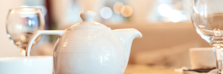 Elegant white teapot on dining table with glasses and warm ambient lighting in cozy setting.