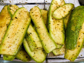 Fresh green zucchini slices marinated in blend of herbs and spices in glass container. Zucchini cut into long pieces, vibrant color and texture. Dish for grilling or roasting, flavor and nutrition