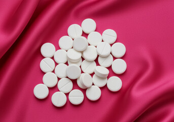 White Pills on Bright Pink Satin Background in Close-Up Studio Shot