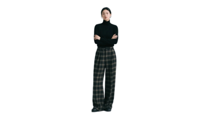 A woman is standing with arms crossed, wearing a black turtleneck and plaid wide-leg pants, showcasing a modern fashion look.