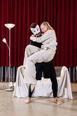 A mime performing a role holds an actress in his arms close-up on a theatre stage.