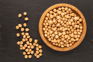 Dry chickpeas in a wooden plate on a slate stone, macro, top view.