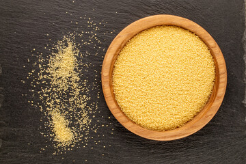 Couscous in a wooden plate on a slate stone, close-up, top view.