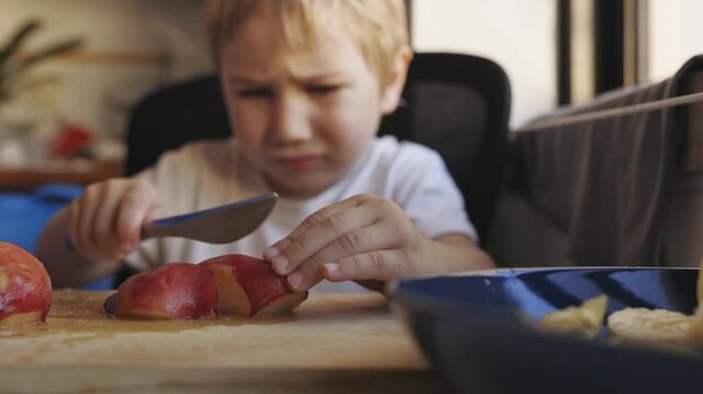 Little boy learning to cut peach with knife