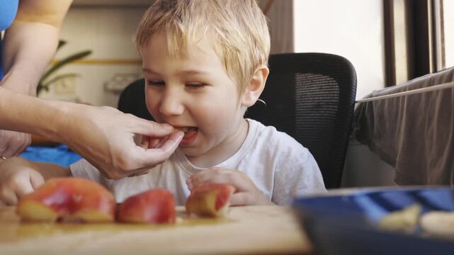 Mother teaching cute little son to cut fruit