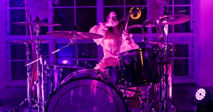 Camera getting closer to beautiful drummer Girl in lush pink dress playing drums in recording studio with large panoramic windows. At the end of the rock show girl lowers her head and stop playing