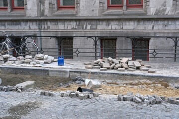 Street renovation in progress, repair work with cobblestone on city street. Road and sidewalk re-laying with visible sand for base square stones in piles
