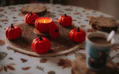 Cozy autumn still life with small pumpkin decorations, a burning candle, and a cup of coffee on a rustic table, creating a warm seasonal and festive atmosphere.