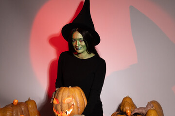 Woman in black dress and witch hat surrounded by glowing pumpkins.