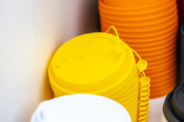Stacked colorful silicone coffee cup lids in yellow, orange, black, and white on a white background, representing eco-friendly kitchenware